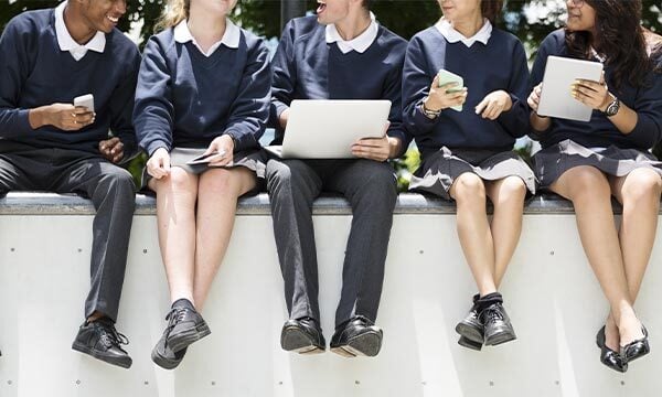 Group of school children sat on a wall using different types of mobile device