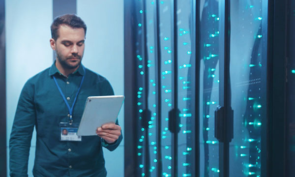 Young IT engineer look at a tablet while walking down a server room