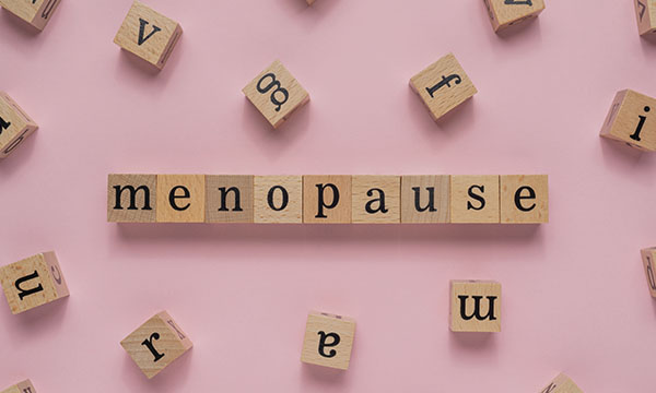 Menopause word on wooden block. Flat lay view on light pink background.