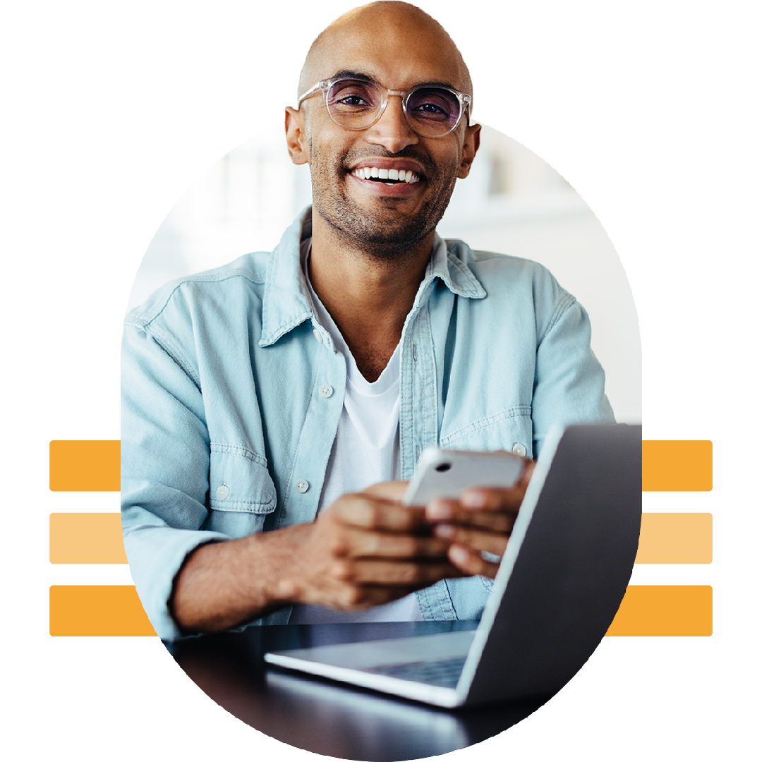 Image of a smiling working professional working on a laptop and holding a mobile phone
