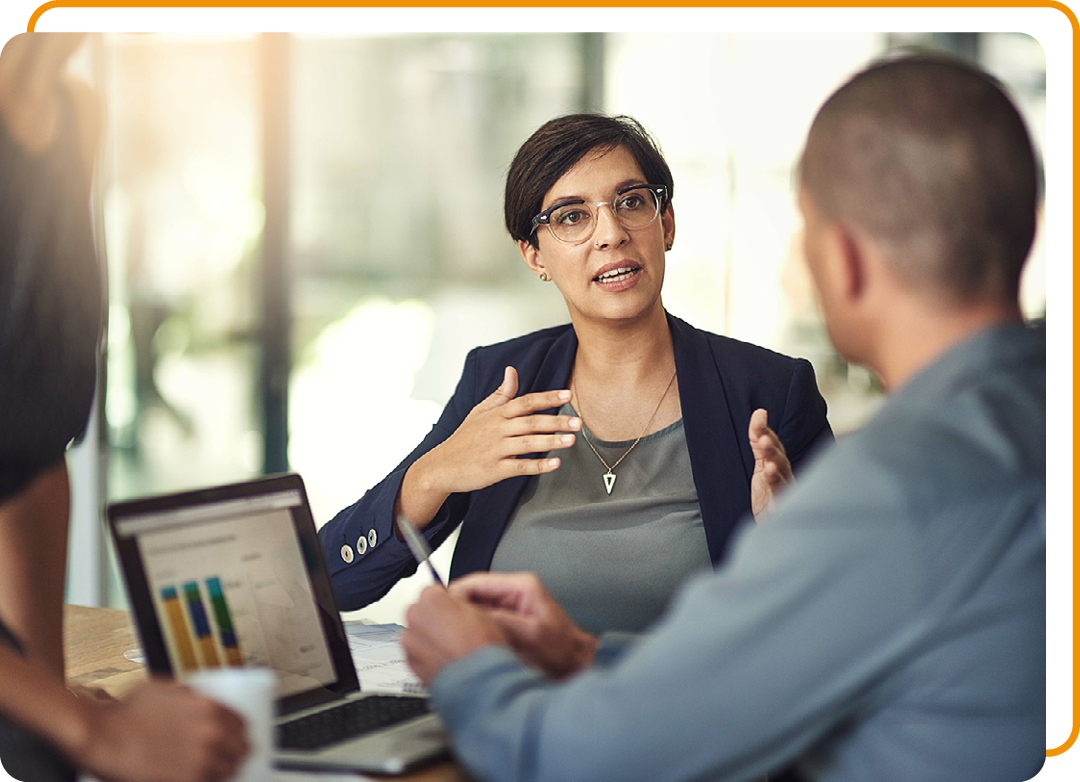 Image of three people with on in focus talking to another one about some results on a laptop screen