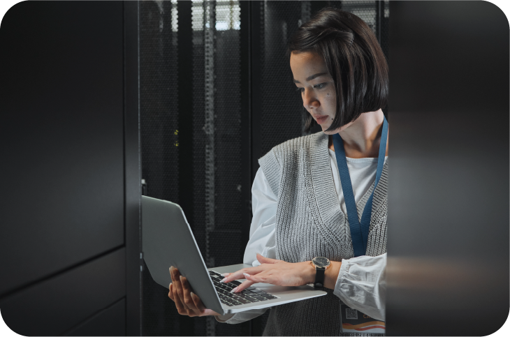 Woman in casual clothes wearing lanyard stood working on laptop in dark office
