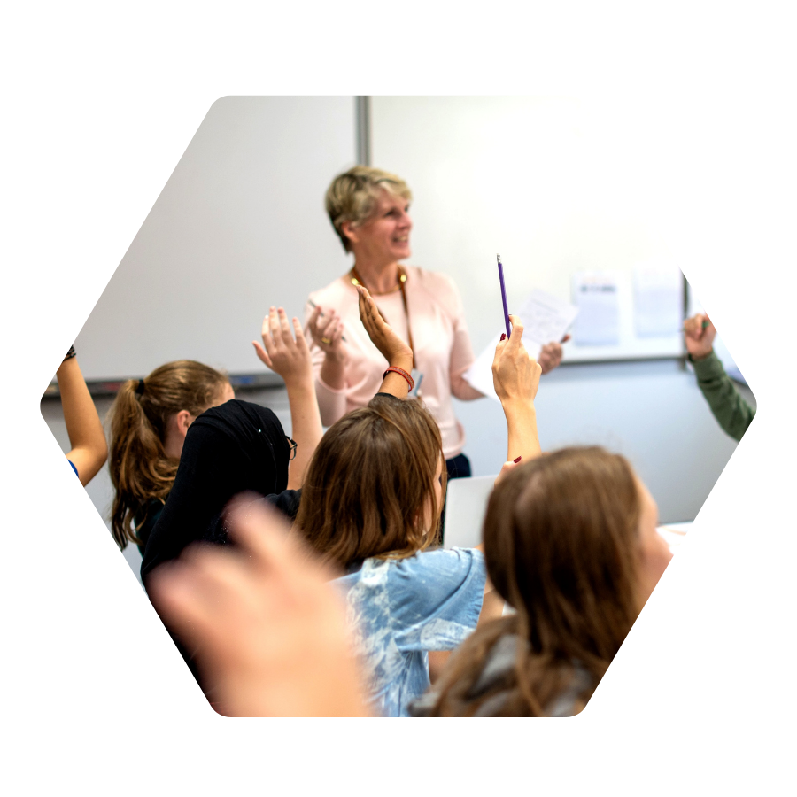 A classroom with students raising hands and a teacher at the front